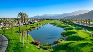 A golf course with a pond, palm trees, and mountains in the background. - Private Pool Home in Highly Sought After Mountain View Country Club (La Quinta)