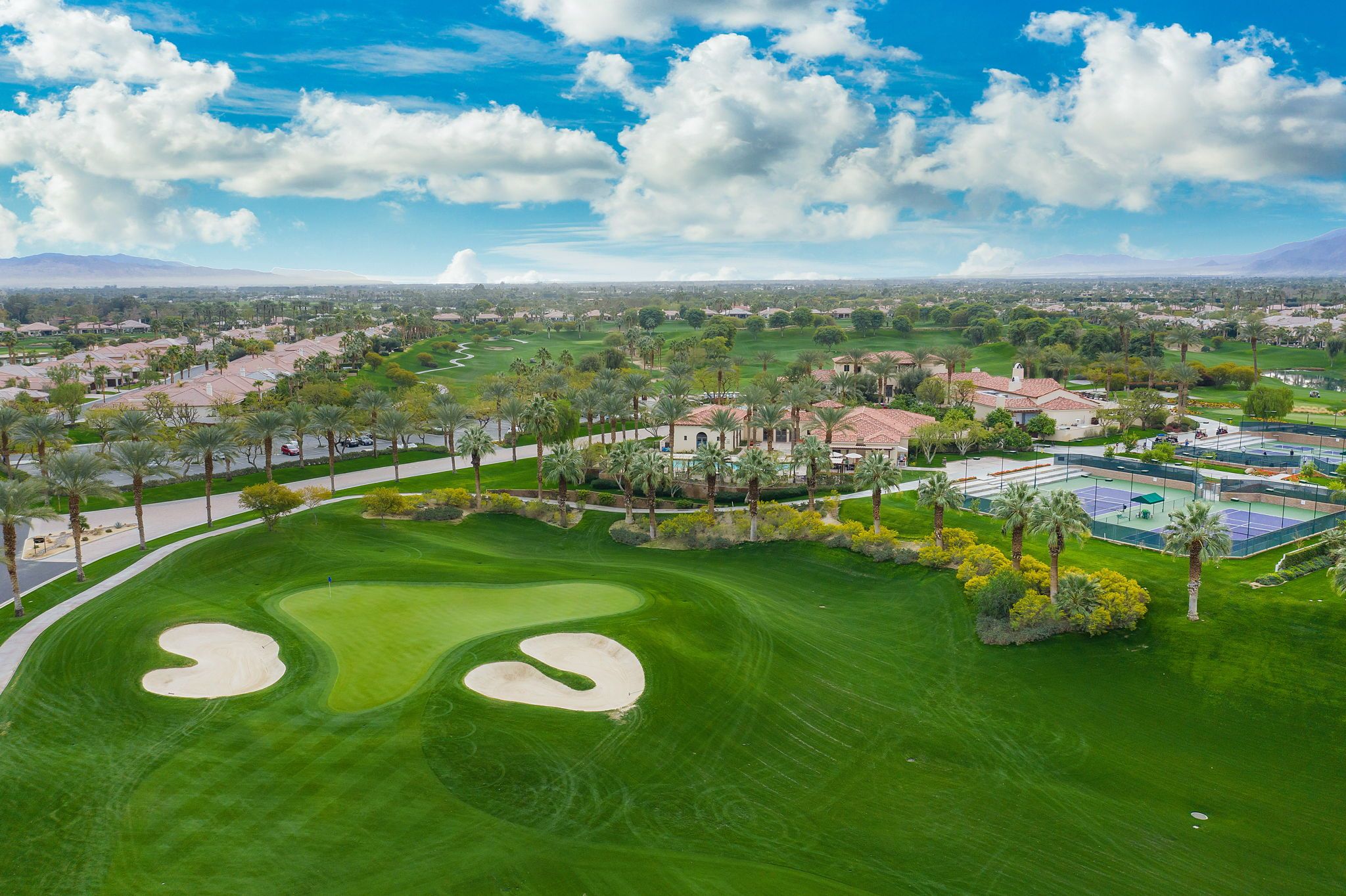 An aerial view of a golf course with sand bunkers, palm trees, and residential buildings in the background.