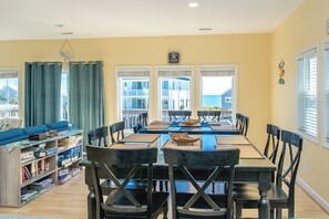A dining area with a table and chairs, a bookshelf, and a view of the ocean. - South Shore Sea Esta - 5 BR Second Row Home - Pool & Kiddie Pool (Surf City)