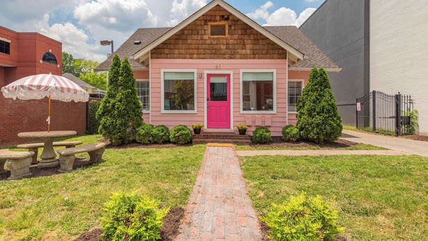 A pink house with a red door, a brick patio, and a small garden.