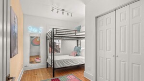 A bedroom with a bunk bed, a colorful rug, a neon sign, and a white door.