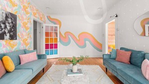 A modern living room with teal sofas, a marble coffee table, and a colorful abstract mural on the wall.