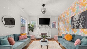 A living room with teal sofas, a round coffee table, a fireplace, and a large TV.