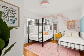 Ein Schlafzimmer mit einem Etagenbett, einem Einzelbett, einem Nachttisch mit Lampe und einer Wand mit Blumenmuster.