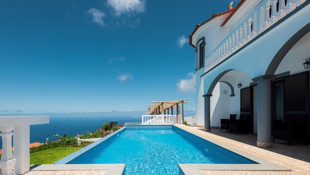 Une piscine avec vue sur la mer, un espace extérieur couvert et un bâtiment agrémenté de colonnes et d’arcades.