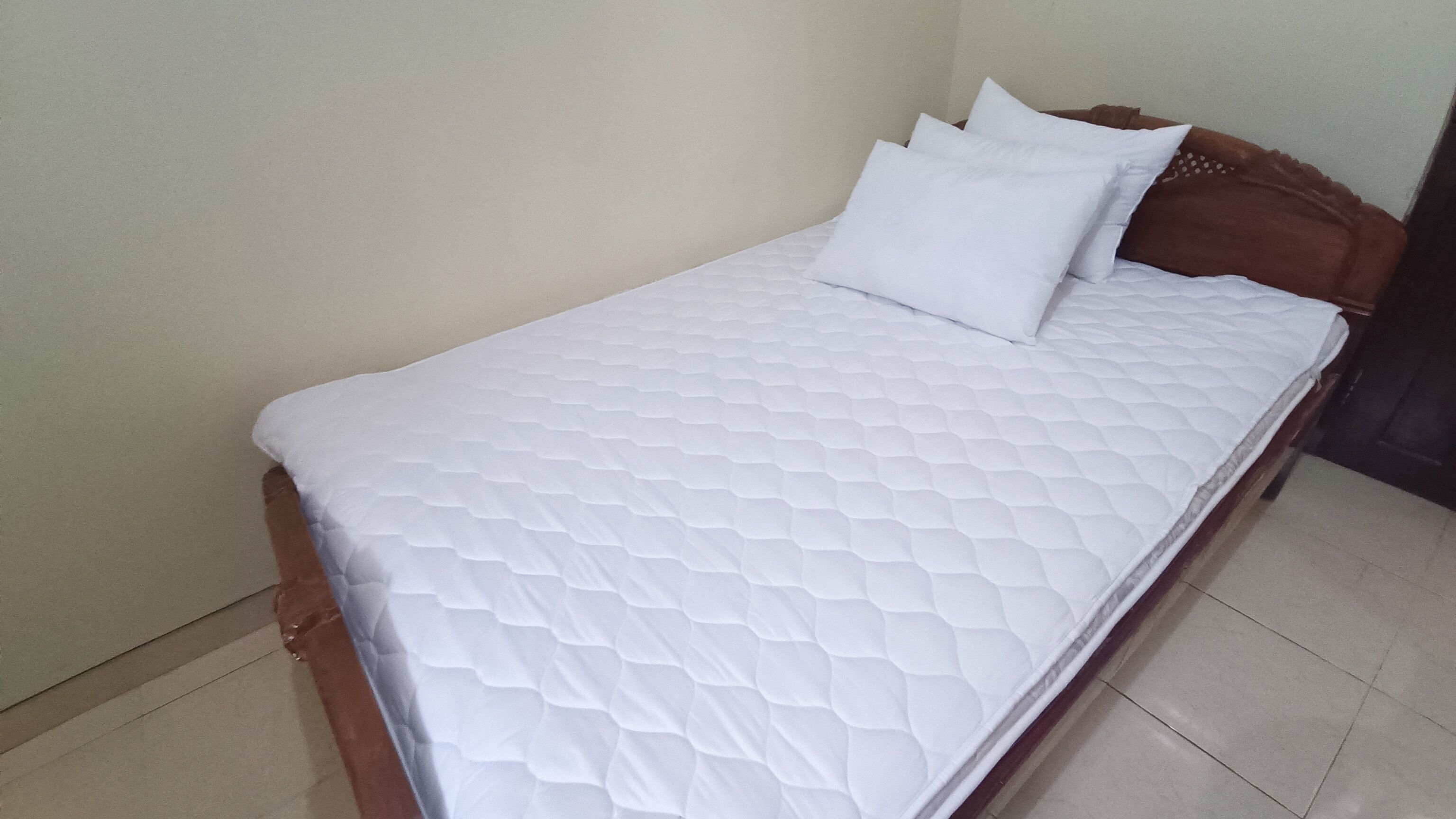 Un lit simple avec un matelas et des oreillers blancs à motifs matelassés, une tête de lit en bois et un mur uni.