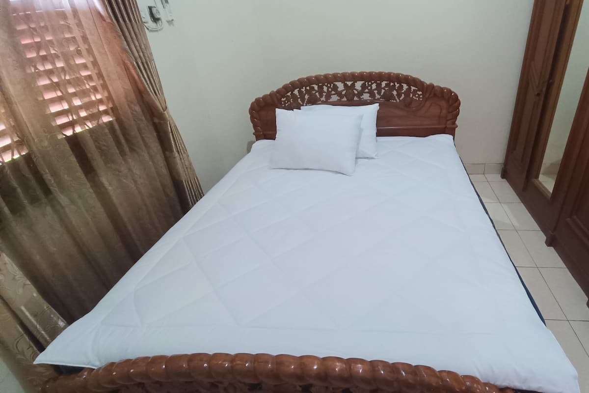 A single bed with a wooden headboard and white bedding in a room with a tiled floor and a wooden door.