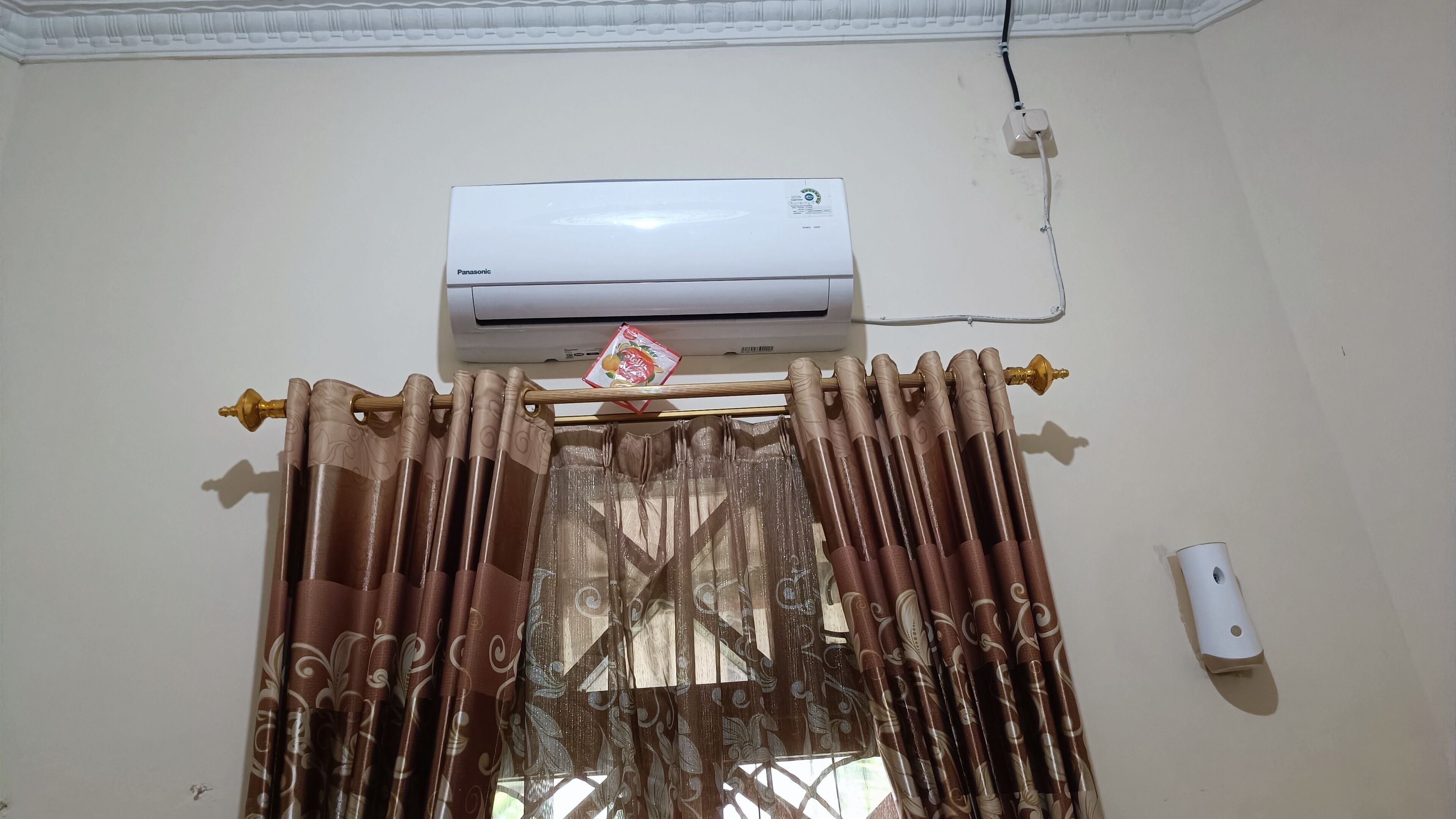 An air conditioning unit mounted on a wall above a window with brown curtains.