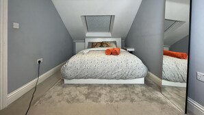 A bedroom with a sloped ceiling, a skylight, a bed with a patterned bedspread, and a mirror reflecting the bed. - Luxurious Double Studio in London (London)