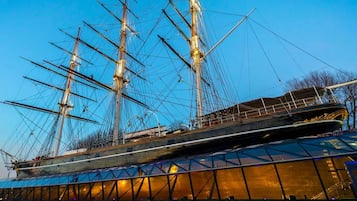 A large ship with multiple masts, docked at a modern building with a glass facade.