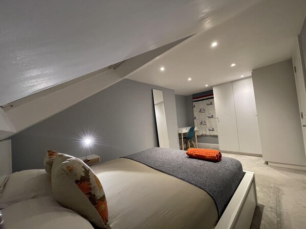 A bedroom with a sloped ceiling, a bed with a floral pillow, a desk, and a wardrobe. - Luxurious Double Studio in London (London)