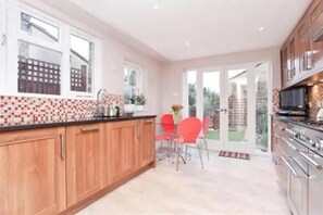 A kitchen with wooden cabinets, a tiled backsplash, a dining area with red chairs, and a sliding glass door leading to a garden. - Luxurious Double Studio in London (London)