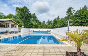 A swimming pool with clear blue water, surrounded by a tiled deck. There are lounge chairs and a small building with windows and a door. - Nice apartment in Ebeltoft with sauna (Ebeltoft)