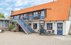 Ein zweigeschossiges Gebäude mit rotem Ziegeldach, blauer Freitreppe und einer Außenbereich-Sitzgelegenheit mit Tischen und Stühlen.