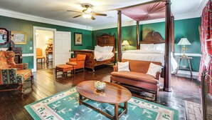 A four-poster bed, a wooden coffee table, a sofa, and a chair in a room with green walls and hardwood floors.