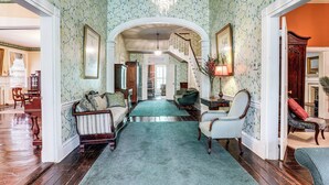 A spacious hallway with a grand staircase, antique furniture, and a chandelier.