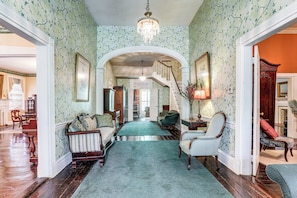 A hallway with a staircase, a chandelier, and a green carpet. - Historic 5,400-sq-ft Woodville Estate w/ Pool (Woodville)