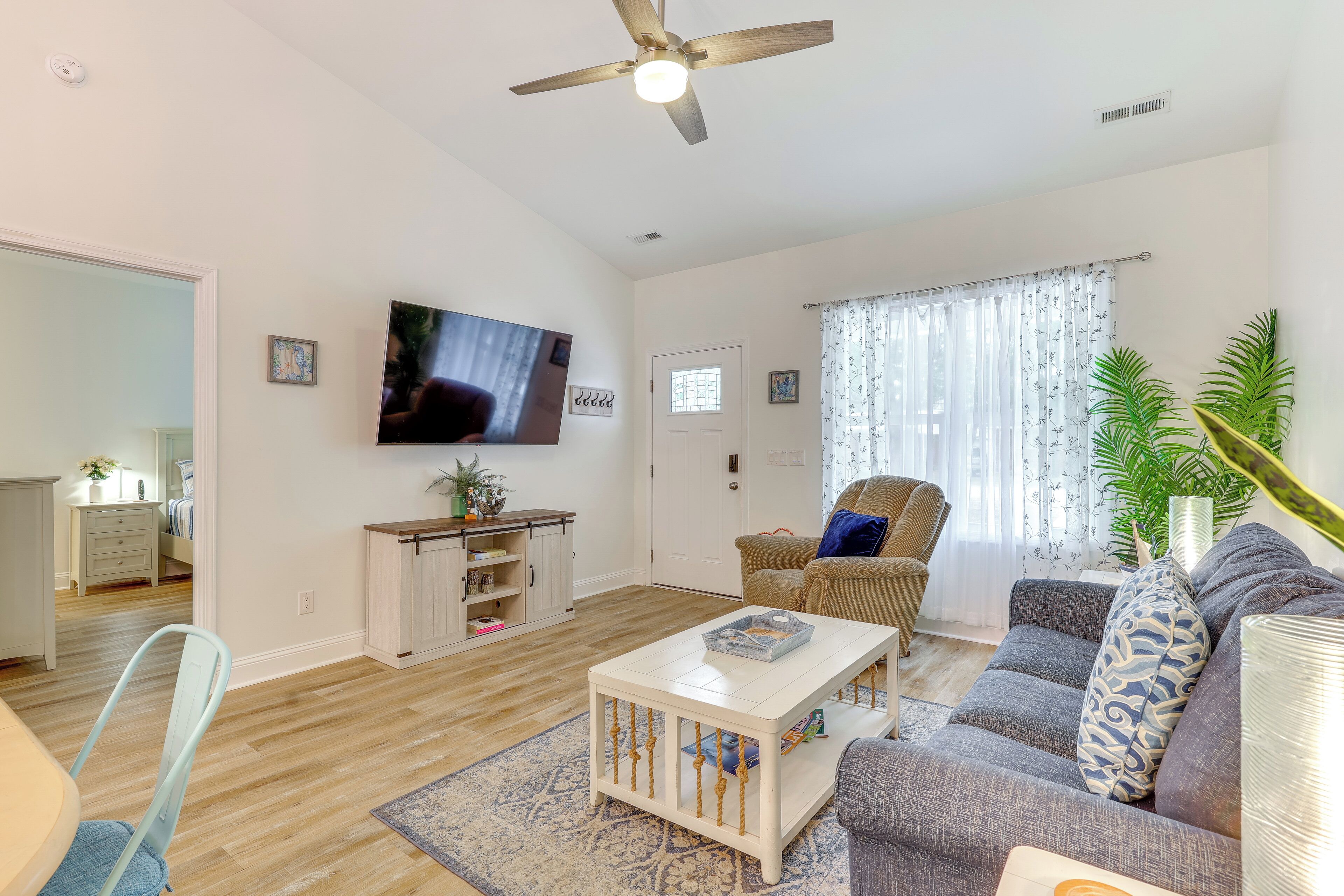 A living room with a television, a ceiling fan, a sofa, a coffee table, and a dining area with a chair and table.