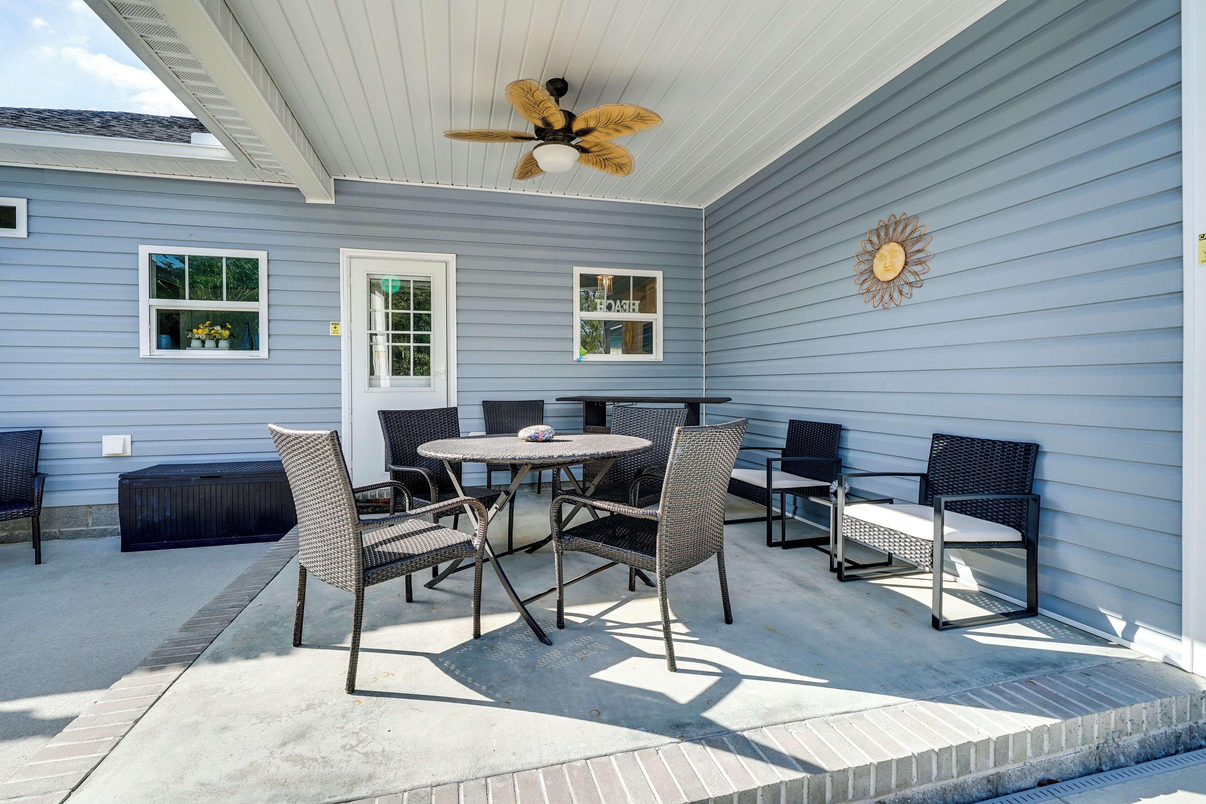 Une terrasse couverte avec un ventilateur de plafond, une table avec des chaises et un soleil décoratif peint sur le mur.