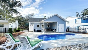 Entorno residencial con piscina, dos sillones de descanso y un porche cubierto.