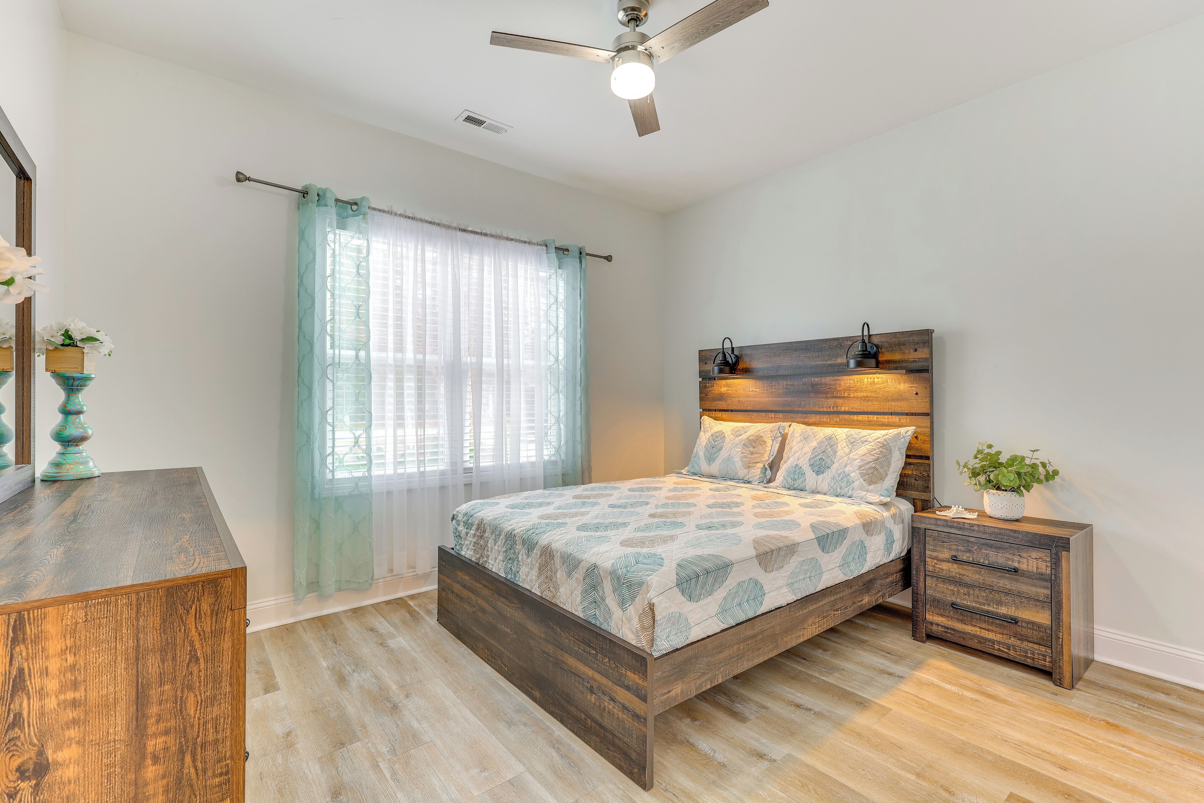 Une chambre à coucher avec un lit en bois, une table de chevet, une commode et un ventilateur de plafond.