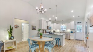 Una cocina moderna con armarios blancos, una isla central y un comedor con una mesa redonda y sillas azules.