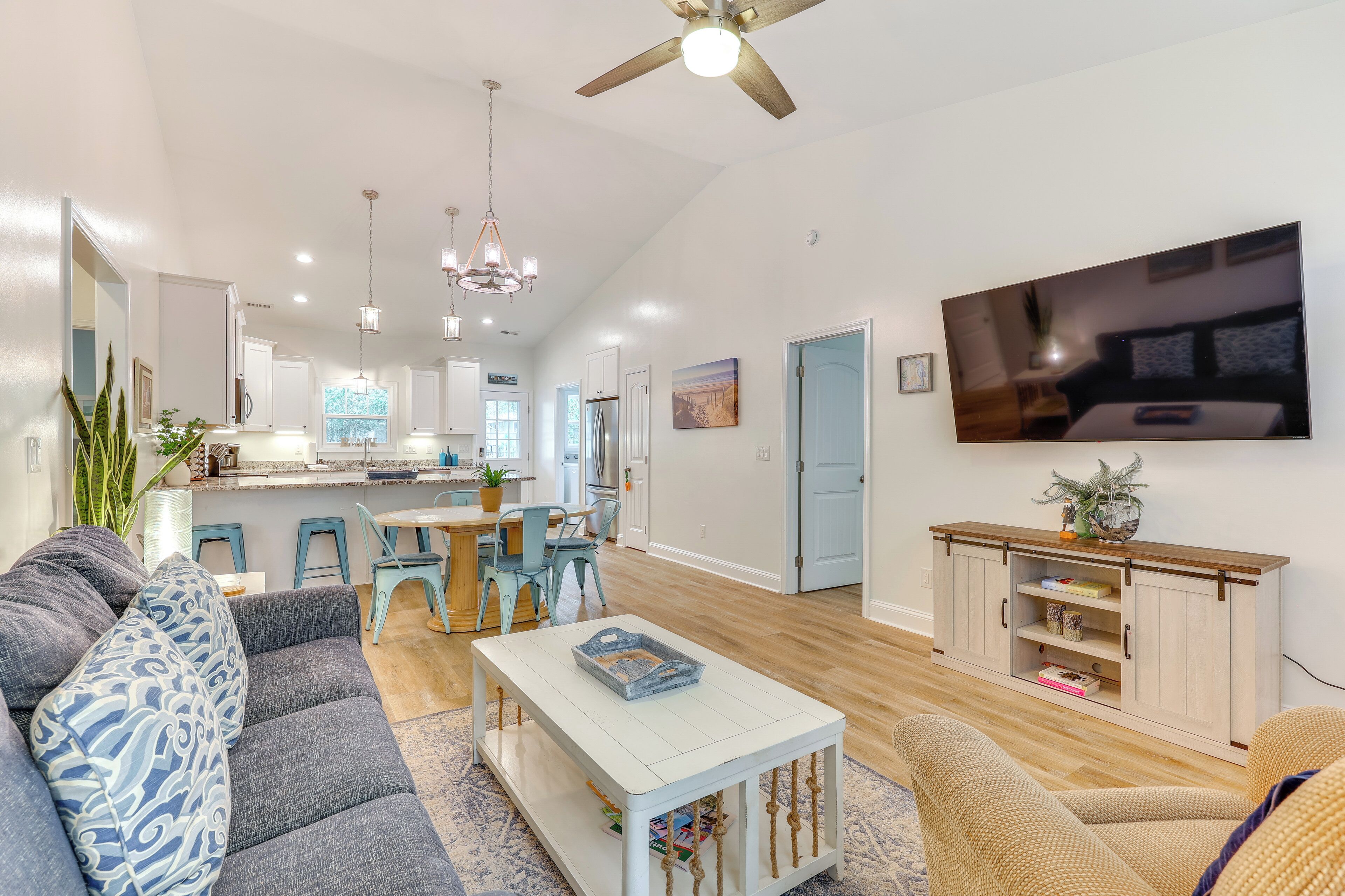 A spacious living room with a grey sofa, a white coffee table, and a TV mounted on the wall.