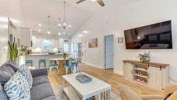 A spacious living room with a grey sofa, a white coffee table, and a TV mounted on the wall.