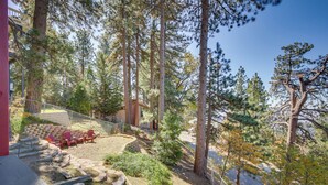 A backyard with a stone patio, red Adirondack chairs, and a wooden deck. - Colorful Running Springs Cabin w/ Incredible Views (Running Springs)