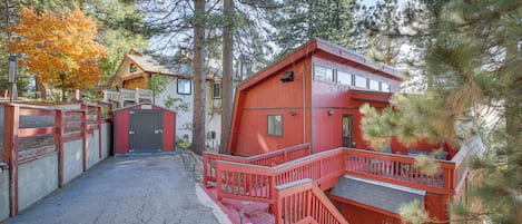 A red wooden building with a porch and a staircase, surrounded by trees.