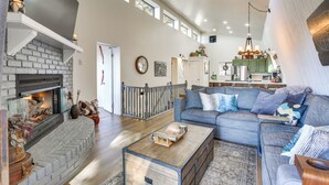 A spacious living room with a fireplace, a blue sofa set, and a kitchen in the background. - Colorful Running Springs Cabin w/ Incredible Views (Running Springs)
