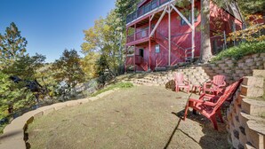 A red building with a balcony, a stone wall, and red Adirondack chairs in a grassy area. - Colorful Running Springs Cabin w/ Incredible Views (Running Springs)