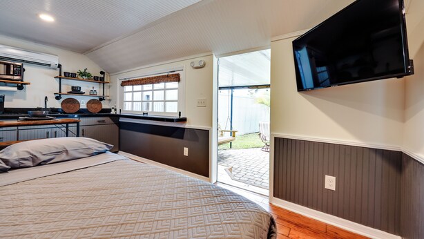Una habitación compacta con cama, kitchenette y televisor montado en la pared.