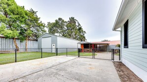 Un patio trasero con un adoquín, una zona vallada y un edificio de techo rojo.