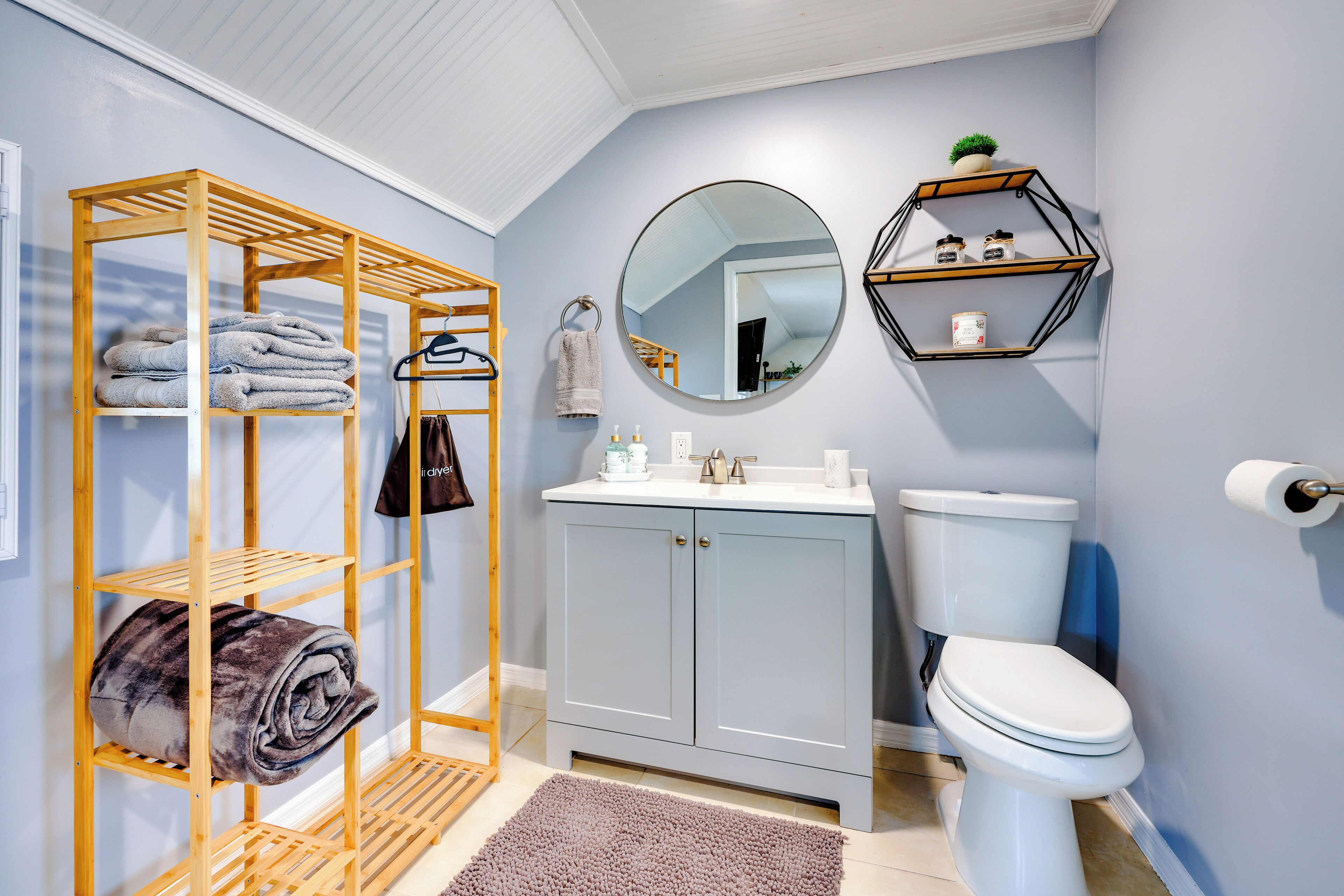 A bathroom with a wooden towel rack, a round mirror, a toilet, and a shelf with toiletries.