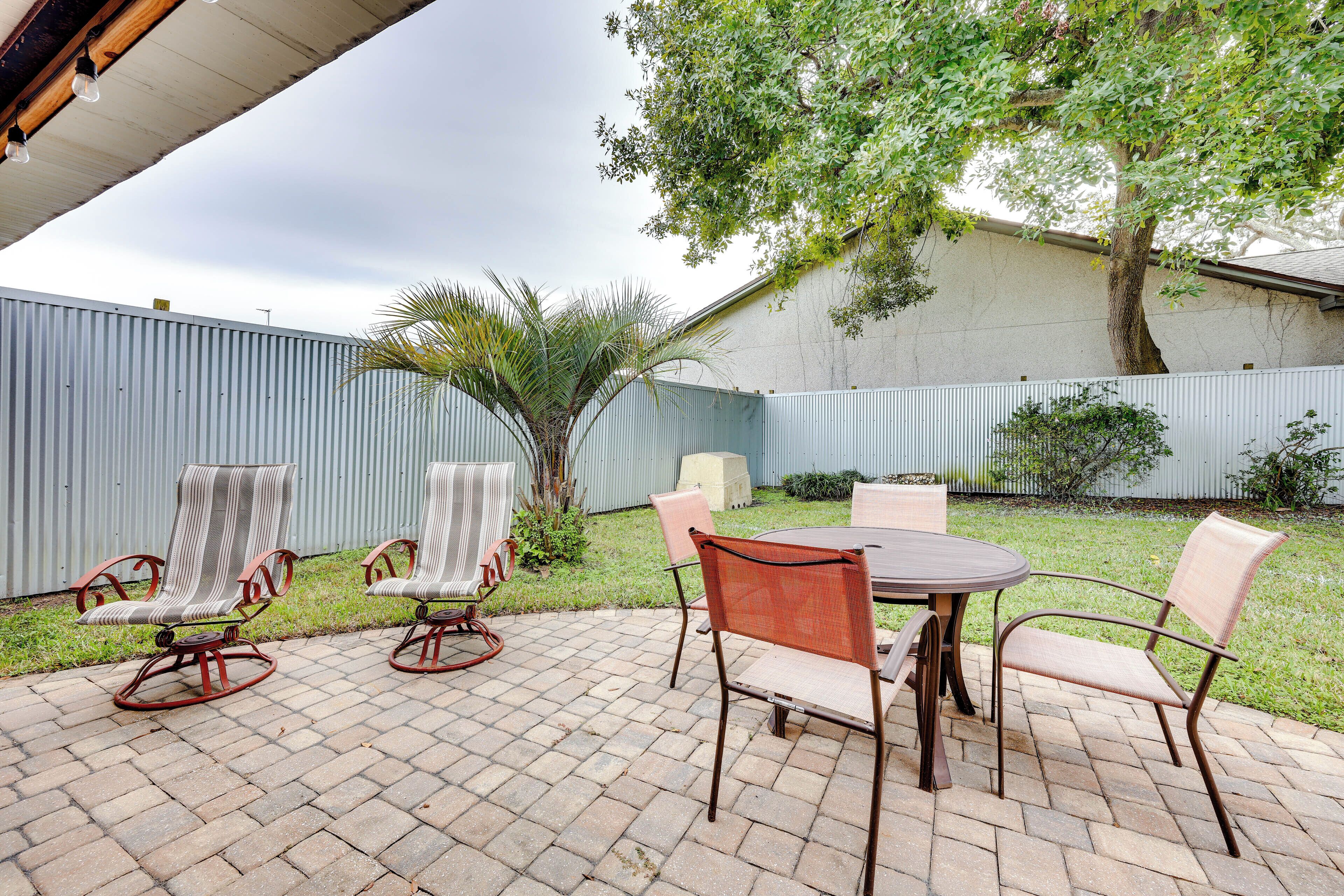 Un patio con mobiliario exterior, incluyendo sillas y una mesa, rodeado de piso de ladrillo y una cerca metálica.