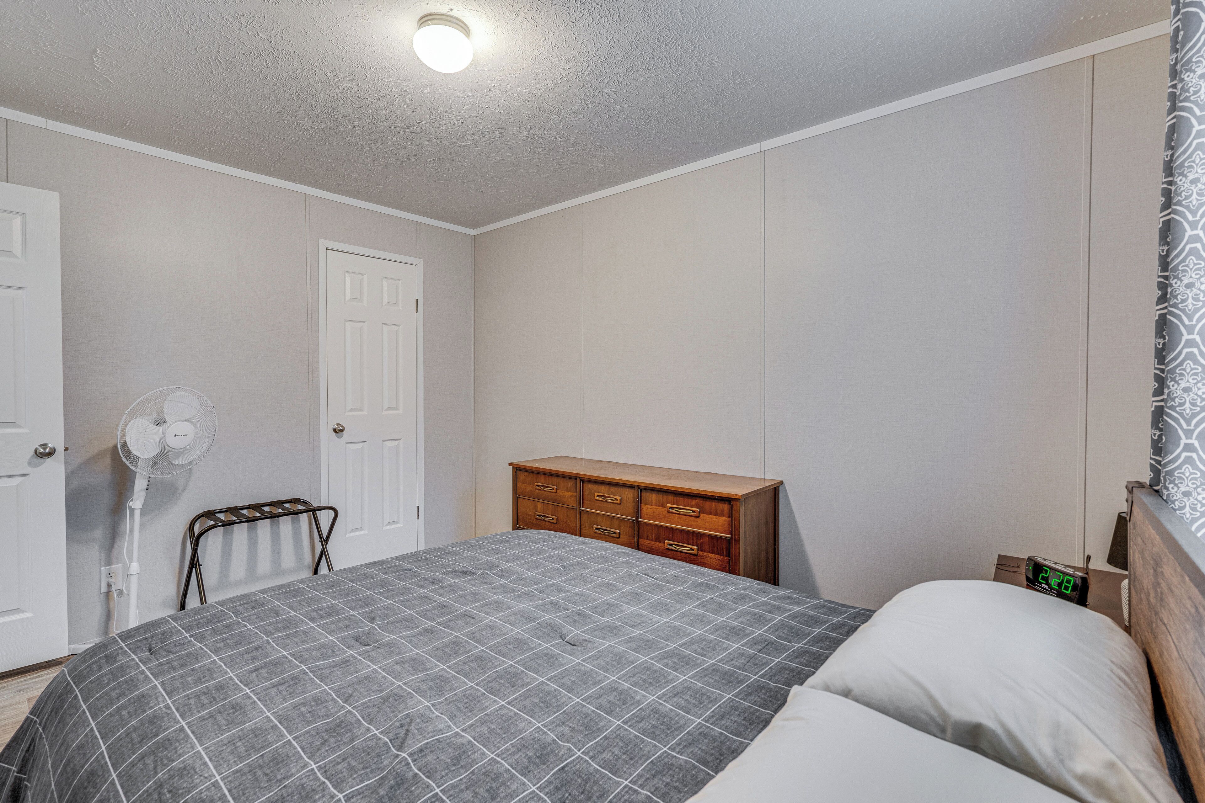 A bedroom with a bed, a dresser, a fan, and a door.