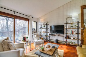 Een moderne woonkamer met een grote televisie, houten vloeren, witte muren en uitzicht op een terras.