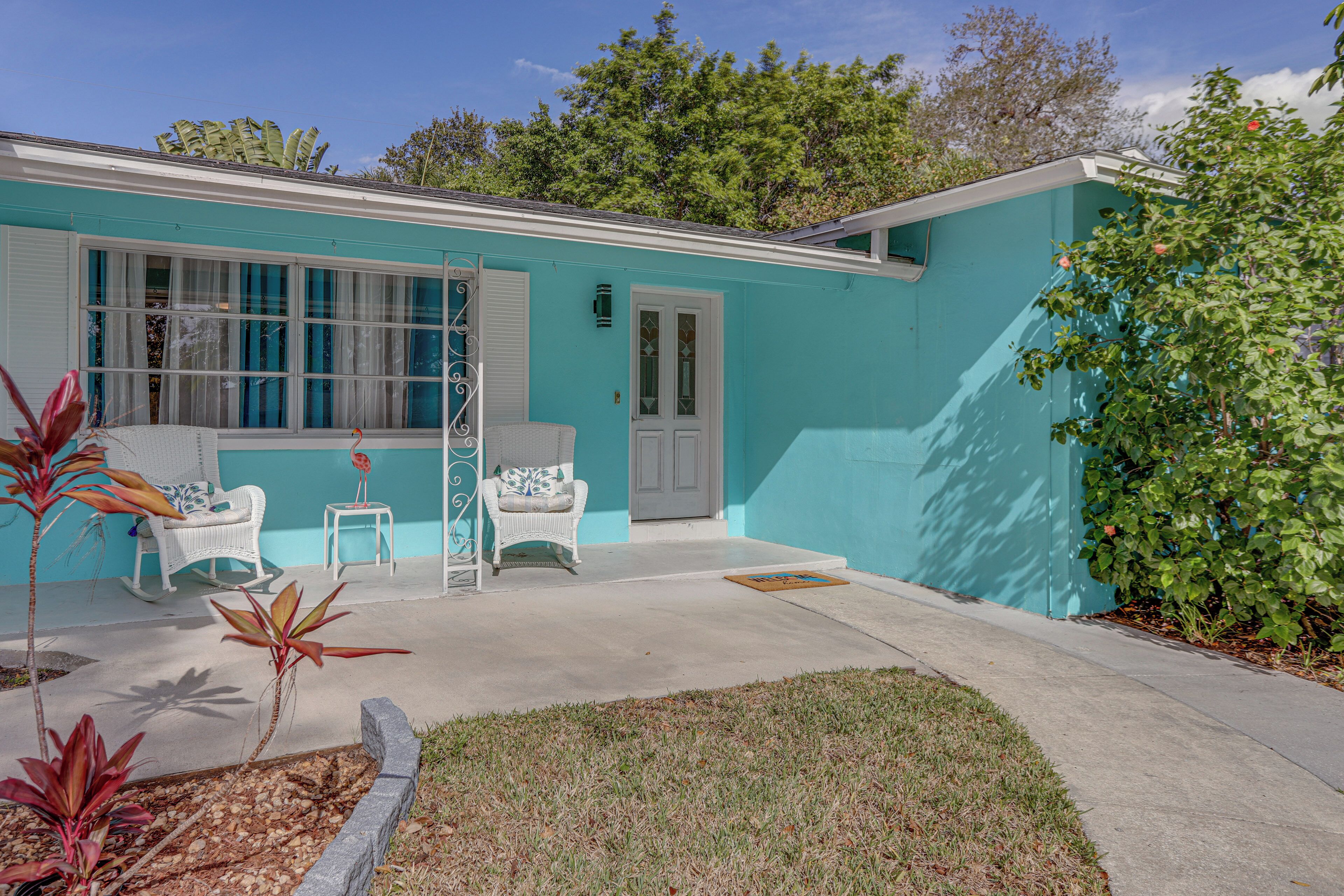 A turquoise house with a garage door, a front porch with two white wicker chairs, and a small side table.