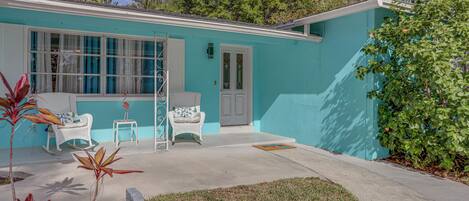 A turquoise house with a garage door, a front porch with two white wicker chairs, and a small side table.