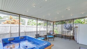 Eine überdachte Terrasse im Freien mit Whirlpool, Korbmöbeln und Blick auf den Garten.