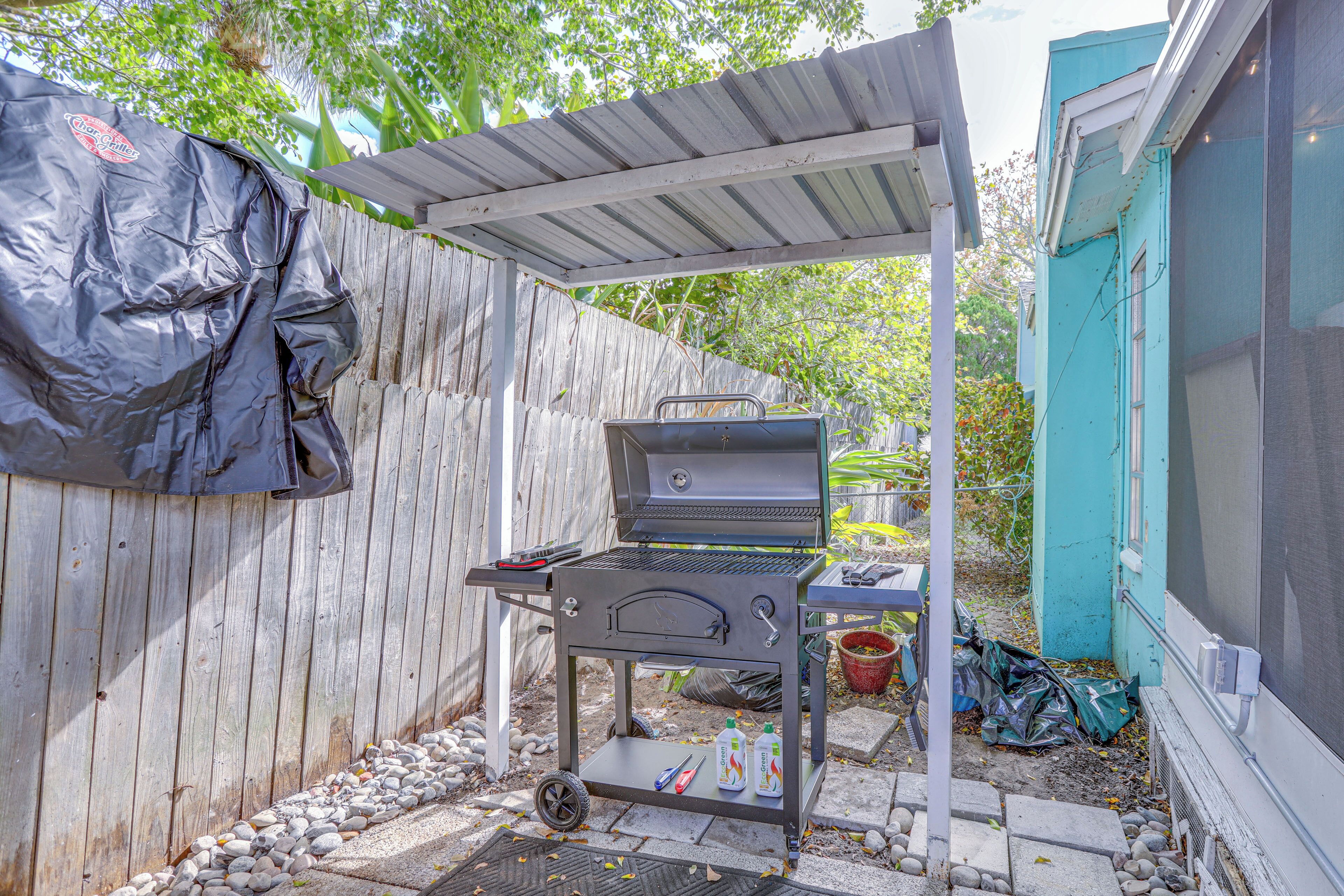 A backyard with a barbecue grill under a pergola, a wooden fence, and a blue building.
