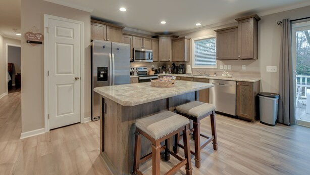 A modern kitchen with wooden cabinets, a stainless steel refrigerator, a microwave, and a large island with bar stools. - Family-friendly Home w/ Deck Near Colonial Beach! (Colonial Beach)