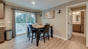 A dining area with a table set for four, a trash can, and a view of the outdoors through a sliding glass door. - Family-friendly Home w/ Deck Near Colonial Beach! (Colonial Beach)