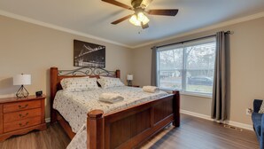 A bedroom with a wooden bed, a ceiling fan, a window with curtains, and a nightstand with a lamp. - Family-friendly Home w/ Deck Near Colonial Beach! (Colonial Beach)