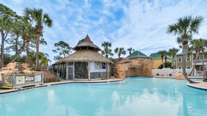 A swimming pool with a thatched-roof structure, palm trees, and a rocky landscape. - Family-friendly Pensacola Home < 1 Mi to Beach! (Pensacola)