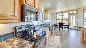 A modern kitchen with wooden cabinets, a stainless steel stove, and a dining area with a table and chairs. - Peaceful Deary Vacation Rental w/ Deck & Views! (Deary)