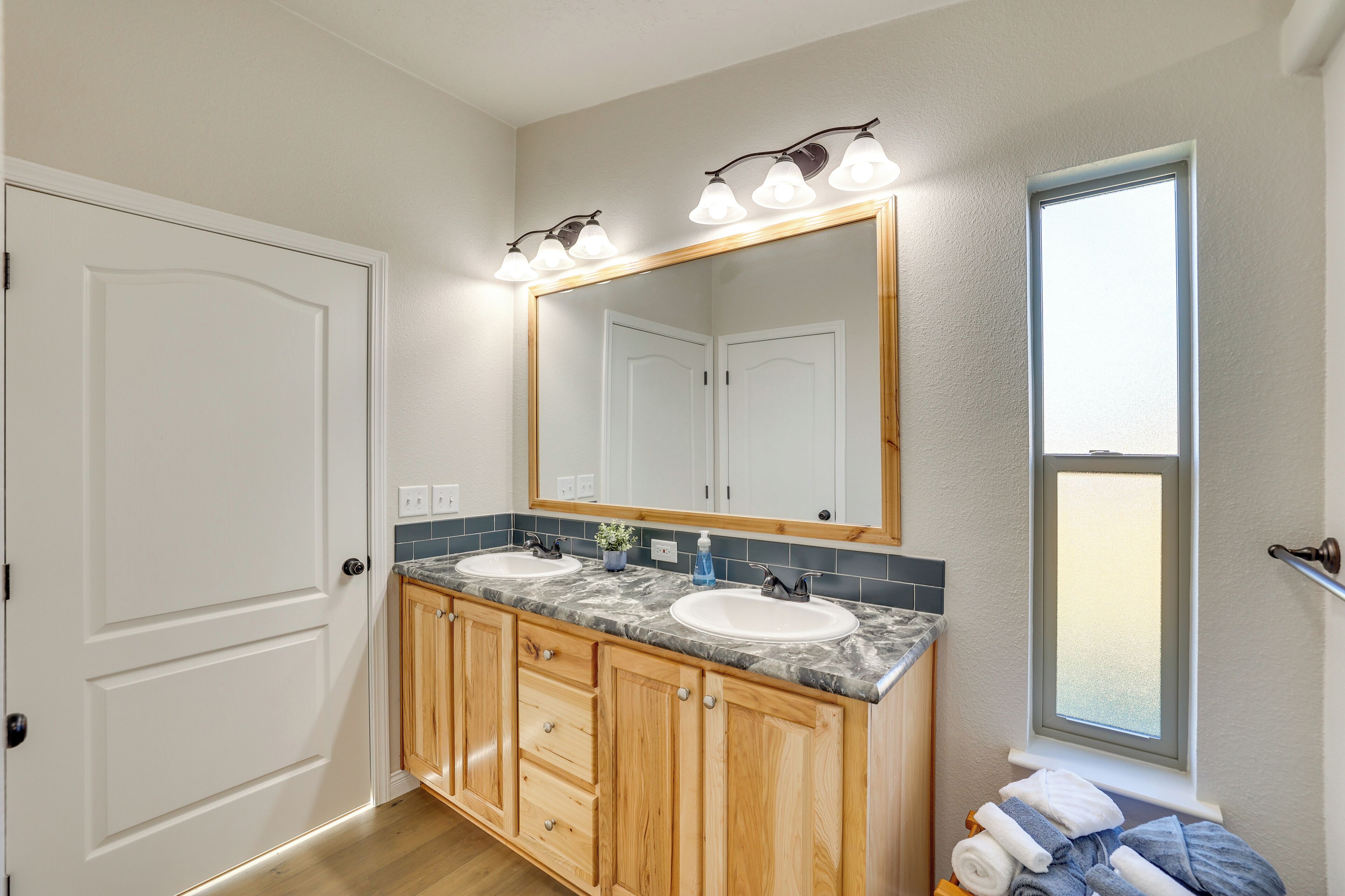 A bathroom with two sinks, wooden cabinets, a large mirror, and a window.