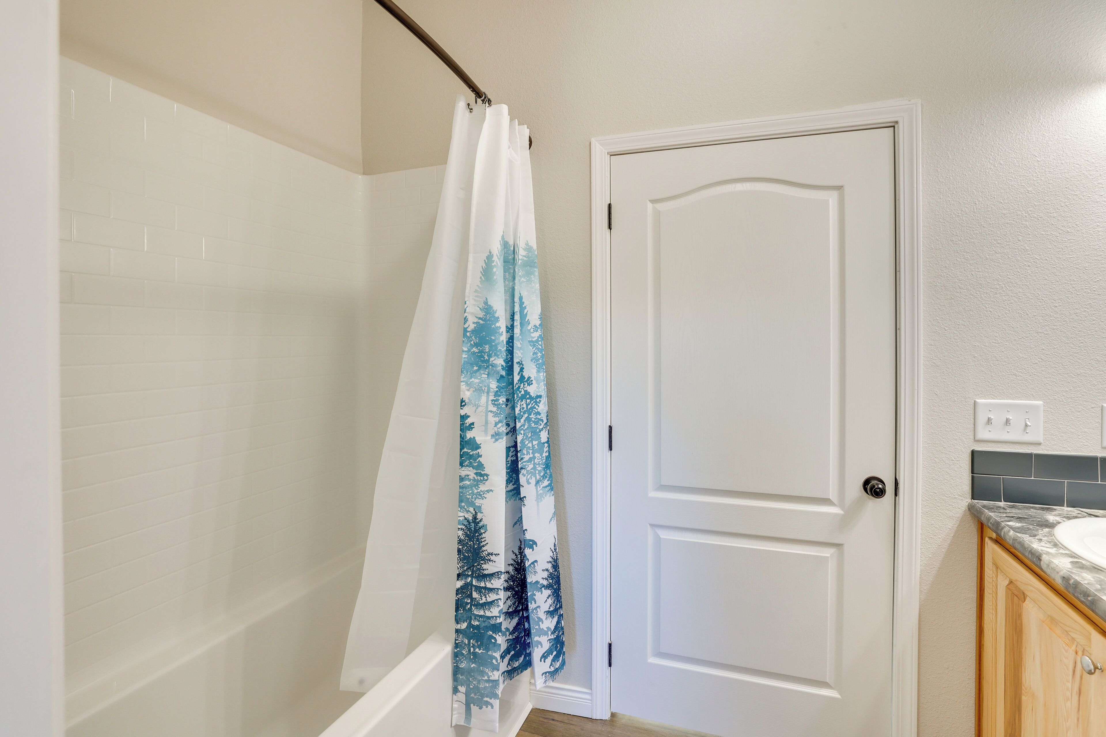 A bathroom with a shower curtain, a white door, and a sink with a marble countertop.