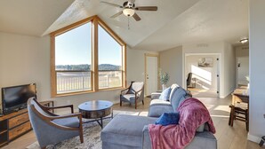 A spacious living room with a large window, a ceiling fan, a gray sofa, and a television. - Peaceful Deary Vacation Rental w/ Deck & Views! (Deary)